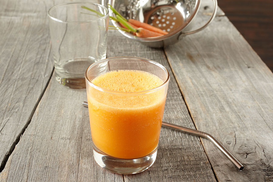 Smoothie de piña y zanahoria en un vaso junto a una pajita