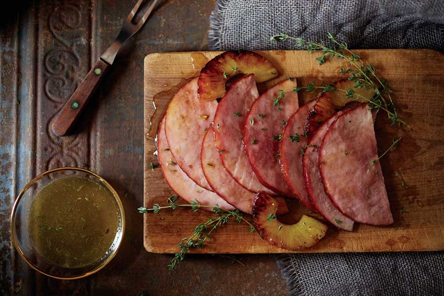 Tabla de madera con jamón glaseado rodajas de piña y tenedor para trinchar