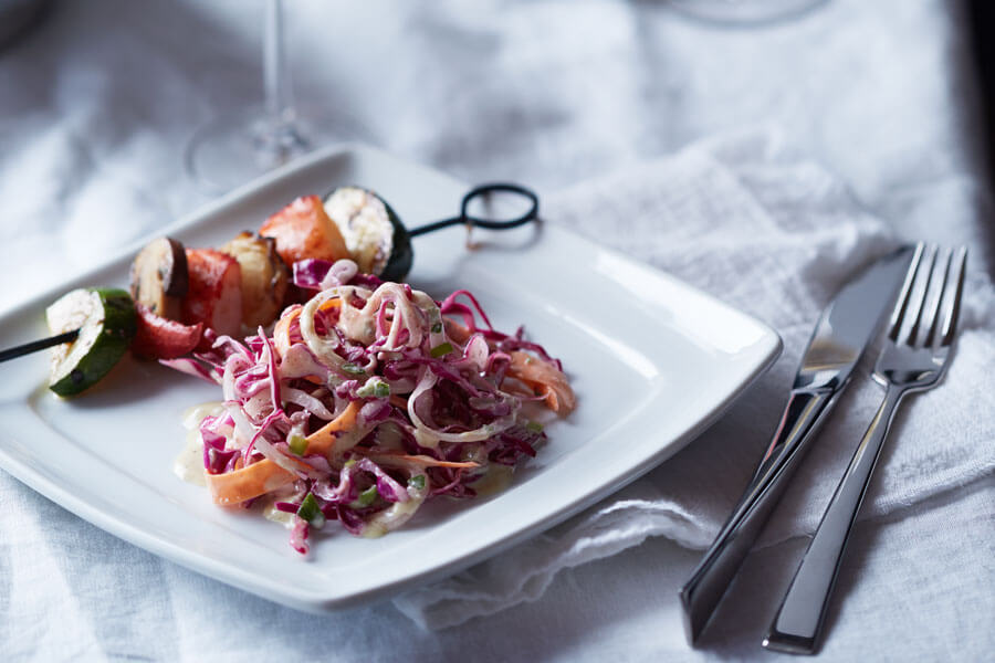 Ensalada de col en un plato junto a una brocheta de verduras