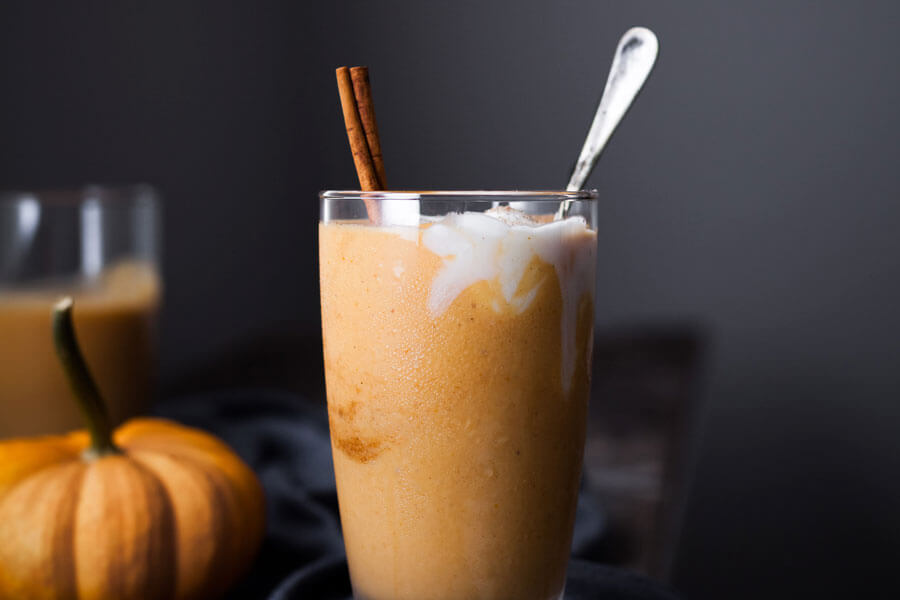 Smoothie de calabaza en un vaso con una ramita de canela y una cuchara.