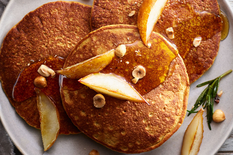 Tortitas con harina de almendra en un plato con manzana, sirope y avellanas partidas