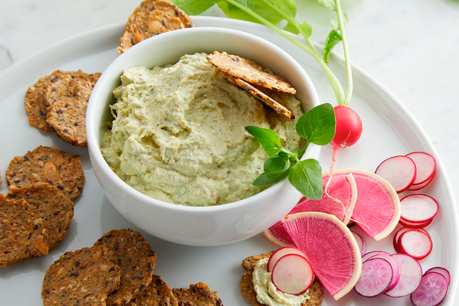 Paté vegano de brócoli y limón en un cuenco con crackers y verduras cortadas